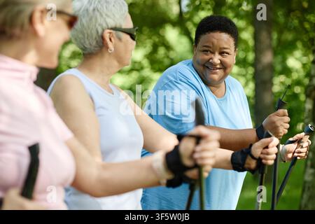 Donna anziana nera sorridente che fa Nordic Walking con amici nel parco Foto Stock