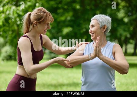 Allenatrice aiuta una donna asiatica anziana con una posa di yoga nel parco Foto Stock