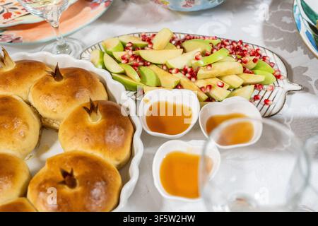 Una tavola festosa mostra pane challah rotondo e mele affettate con miele a lato. Ci sono semi di melograno sulle mele. Fa parte delle tradizioni di Rosh Hashanah. Foto Stock