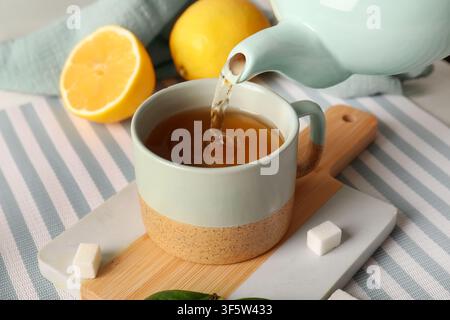 Tè caldo versato da una teiera azzurra in una tazza di ceramica con limone e cubetti di zucchero Foto Stock