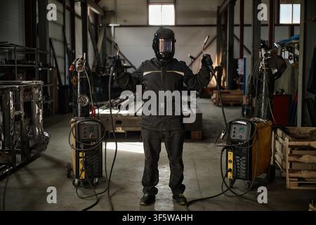 Ritratto di un saldatore con maschera protettiva che tiene delle torce in officina Foto Stock