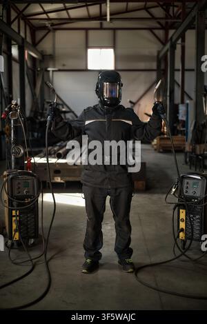 Ritratto di un saldatore con maschera protettiva che tiene due torce in fabbrica Foto Stock