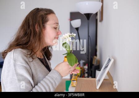 Donna che tiene una mini orchidea in vaso, annusando i suoi fiori delicati all'interno Foto Stock