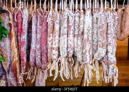 Primo piano di autentici salumi catalani tradizionali, tra cui fuet, llonganissa e pancetta, appesi in esposizione in un mercato locale rustico. Naturale Foto Stock