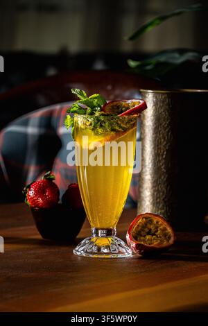 Succo di frutti della passione ghiacciato guarnito con menta fresca e mezze frutti della passione, su un tavolo di legno con fragole e una brocca di metallo incisa. Foto Stock