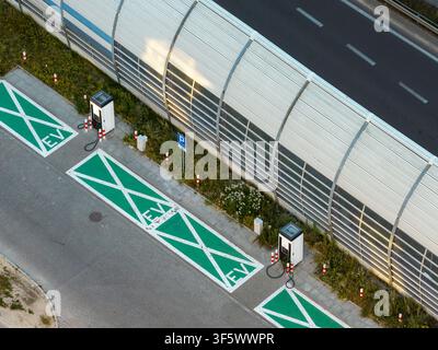Vista aerea di una stazione di ricarica per auto elettriche con posti parcheggio verdi e punti di ricarica situati lungo un muro antirumore a Varsavia, Voivodato della Masovia Foto Stock