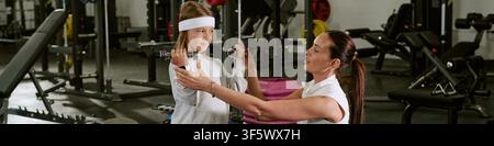 Intestazione di istruttrice donna che guida un bambino nel sollevamento di manubri in palestra Foto Stock