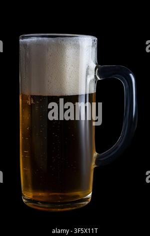 Una tazza di birra in vetro chiaro mostra bolle che salgono in superficie con schiuma in cima. Lo sfondo scuro evidenzia il colore della bevanda. Foto Stock