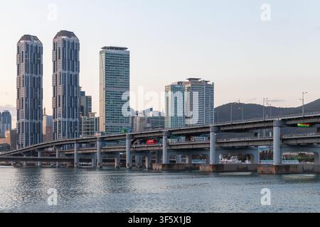 Busan, Corea del Sud - 16 marzo 2018: Paesaggio urbano moderno con grattacieli alti, un ponte su acque calme e uno sfondo montuoso durante il crepuscolo Foto Stock