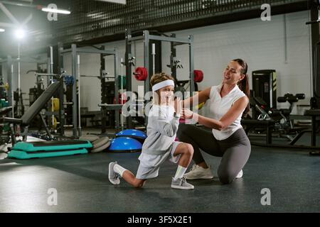 Allenatrice che aiuta un bambino felice a fare fendenti in palestra Foto Stock