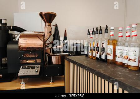 Belgrado, Serbia – 29 luglio 2026. Macchina per la tostatura del caffè accanto a bottiglie di sciroppi aromatizzati Monin e 1883 esposte su un bancone del caffè durante una bevanda Foto Stock