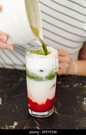 Matcha appena preparato versato su latte freddo per creare vivaci strati verdi in un latte freddo. Bevanda moderna da caffè assemblata a mano. Foto Stock