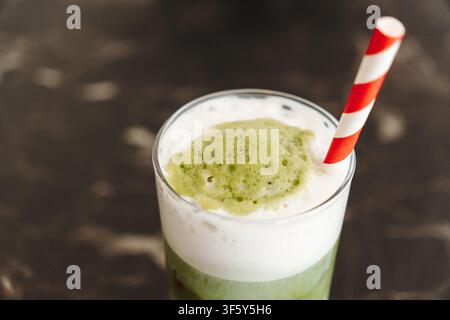 Prima vista di un latte ghiacciato allo matcha e fragola a strati, ricoperto di schiuma cremosa e una cannuccia di carta a righe. Bevanda rinfrescante da caffetteria speciale con vivace Foto Stock