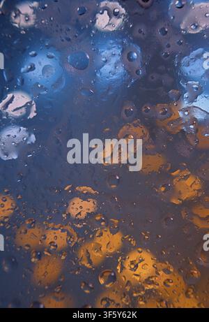 Una scena d'interno suggestiva con gocce d'acqua che si condensano su una superficie di vetro, catturata in un primo piano che enfatizza la trama atmosferica e i Foto Stock