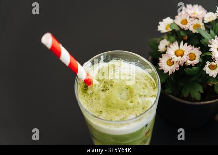 Vista dall'alto di un latte ghiacciato allo matcha con fragola a strati accanto a fiori in fiore su un tavolo scuro. Bevanda rinfrescante da caffè speciale con elegante Foto Stock