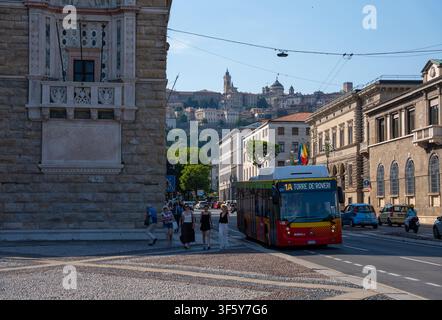 Bergamo, Italia – 16 giugno 2026: Autobus pubblico che procede lungo una strada urbana nella parte bassa di Bergamo con edificio storico in pietra, pedoni e vista sulla Citta Alta Foto Stock