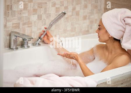 Donna che si gode un rilassante bagno schiuma con doccia Foto Stock