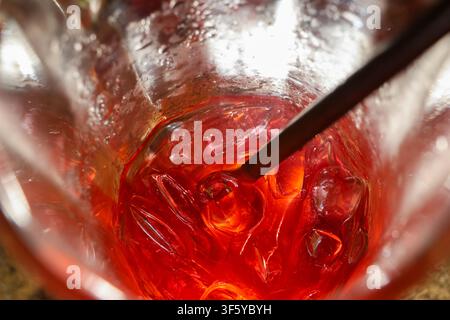 Un cocktail rosso con ghiaccio e cucchiaio da mescolare nel bicchiere, bevanda fredda rinfrescante con riflessi luminosi e colori vivaci Foto Stock