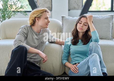 Fidanzato premuroso che consola una giovane donna triste di 18 anni seduta per terra a casa Foto Stock