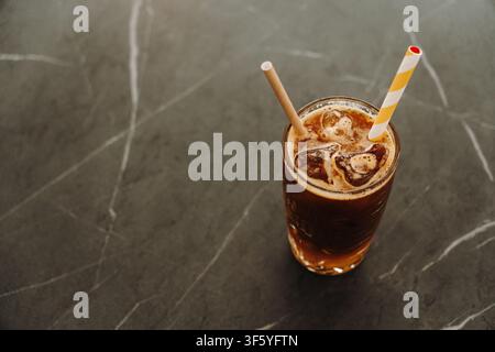 Vista dall'alto di un caffè freddo a strati con succo d'arancia e cannuccia di carta. Caffè speciale rinfrescante servito in un bicchiere decorativo. Foto Stock