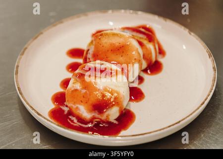 Pancake al formaggio cottage dorati serviti con condimento cremoso e salsa di fragole su un piatto di ceramica. Colazione o dessert fresco fatto in casa in un moderno Foto Stock