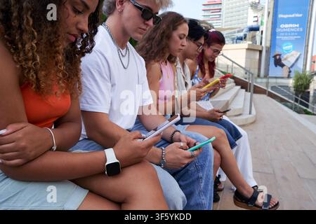 Gruppo multietnico di amici seduti all'esterno tramite telefono cellulare. Foto Stock