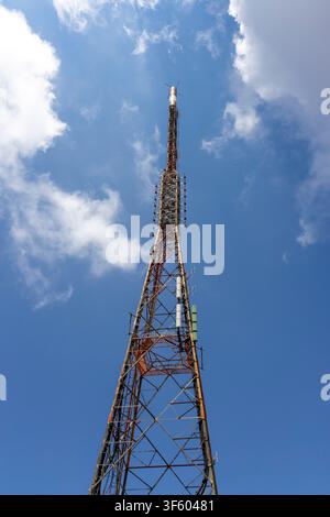 Torre di telecomunicazione che si erge alta contro un cielo blu con nuvole bianche, fornendo servizi essenziali di trasmissione e comunicazione mobile Foto Stock