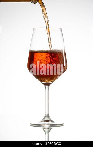 Vino rosato che viene versato in un bicchiere da vino, creando bolle effervescenti su uno sfondo bianco Foto Stock