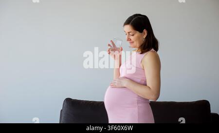 Donna incinta che beve acqua, rimane idratata e gode della maternità Foto Stock