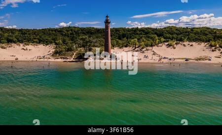 Vista aerea del faro di Little Sable Point sulle dune sabbiose del lago Michigan, circondato da alberi e acqua turchese con persone sulla spiaggia in Foto Stock