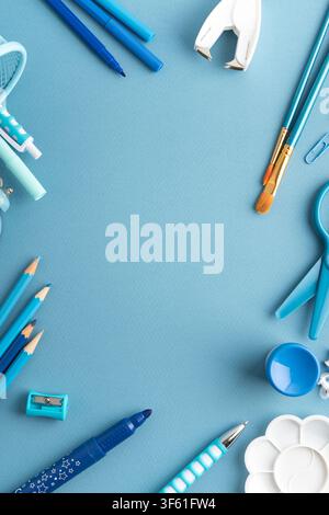 Composizione flat lay con vari articoli d'arte e scolastici blu tra cui penne, matite, pennelli, forbici e una spillatrice su uno sfondo texture Foto Stock