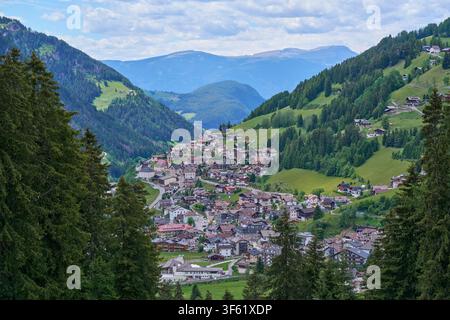 Vista aerea di un villaggio alpino incastonato in una valle montana con colline verdi e una foresta fitta. Foto Stock