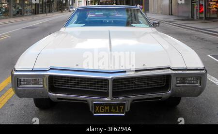 Un piano frontale di un'auto di lusso classica Buick Riviera bianca del 1968 parcheggiata su una strada cittadina. La fotografia evidenzia il suo iconico muso appuntito, l Foto Stock