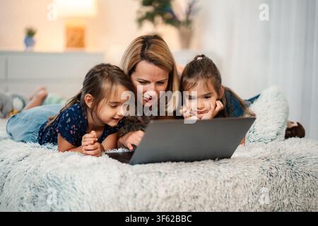 Famiglia che passa un momento felice insieme guardando un laptop a letto Foto Stock