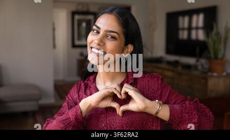 Donna sorridente che fa un gesto cardiaco con le mani Foto Stock