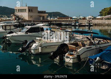Yacht di lusso e barche a vela ormeggiate in una marina sulla costa adriatica del Montenegro. Riva estiva tranquilla con riflessi sull'acqua blu cristallina. Foto Stock
