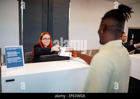 Agente di compagnia aerea che consegna passaporto e carta d'imbarco al passeggero al check-in dell'aeroporto Foto Stock
