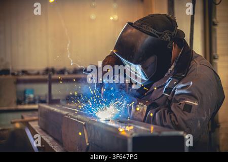 Saldatore professionale che manufactura un componente metallico con scintille e luce luminosa dell'arco di saldatura in fabbrica Foto Stock