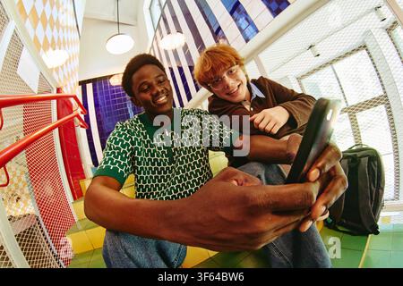 Uomo nero e amico seduti sulle scale e che guardano uno smartphone Foto Stock