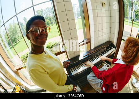 Ritratto di una donna nera che sorride durante una lezione di musica con un collega che suona il pianoforte Foto Stock