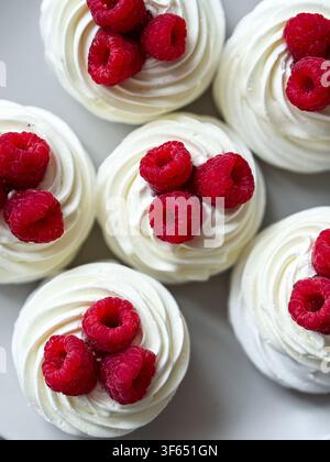 Mini dolci al pavlova con meringa ricoperti di panna montata e lamponi freschi Foto Stock