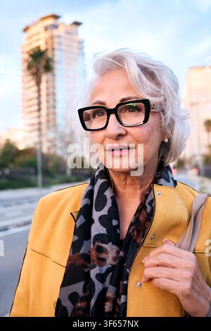Elegante donna anziana che cammina in città al crepuscolo, godendosi la pensione Foto Stock