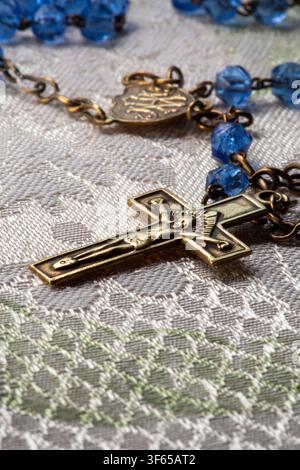 Natura morta di un rosario vintage con un crocifisso in ottone e perle di preghiera in cristallo blu. Foto Stock