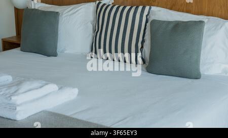 Letto matrimoniale rifatto con lenzuola bianche, cuscini lavorati a maglia verde salvia e asciugamani piegati contro una testiera in quercia — Camera d’albergo, affitto per le vacanze Foto Stock