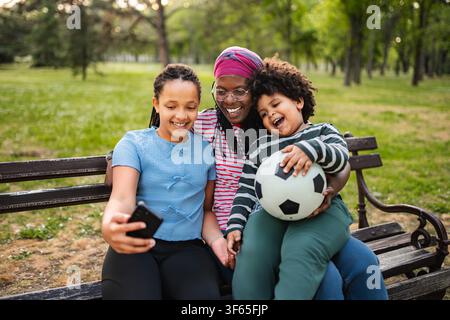 Madre e figli che si scattano un selfie mentre si legano al parco Foto Stock