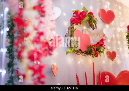 Scatto a fuoco morbido di elementi decorativi per San Valentino, ghirlanda romantica festosa e ghirlanda di cuori di legno appesa al muro con luci bokeh. Foto Stock