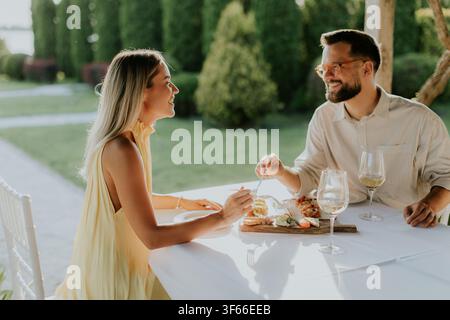 Una coppia condivide risate e cibo delizioso in un incantevole ambiente all'aperto durante il tramonto. La loro conversazione è calorosa e accogliente. Foto Stock