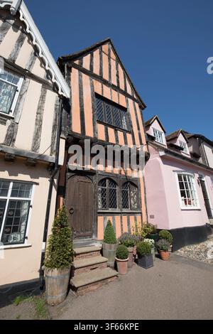 Affascinanti edifici in legno medievale su High Street a Lavenham, Suffolk, con una facciata dipinta di arancione e una antica porta in legno intagliato. Foto Stock