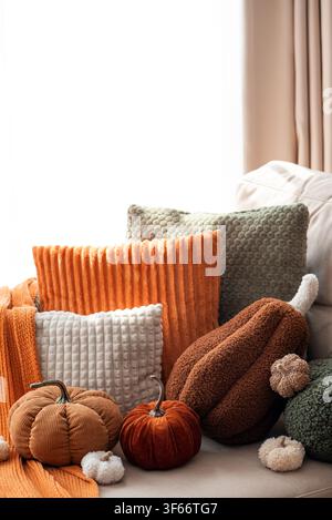 Cuscini dalla trama morbida e zucche di peluche disposte su un divano. Una calda tavolozza autunnale, trame confortanti e una luce gentile evocano un'atmosfera hygge. Foto Stock
