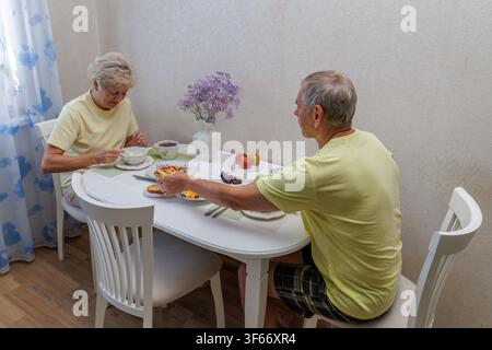 Vista ad angolo alto di una coppia matura felice seduta a un tavolo della cucina e che fa una colazione sana con farina d'avena e uova insieme. Foto Stock